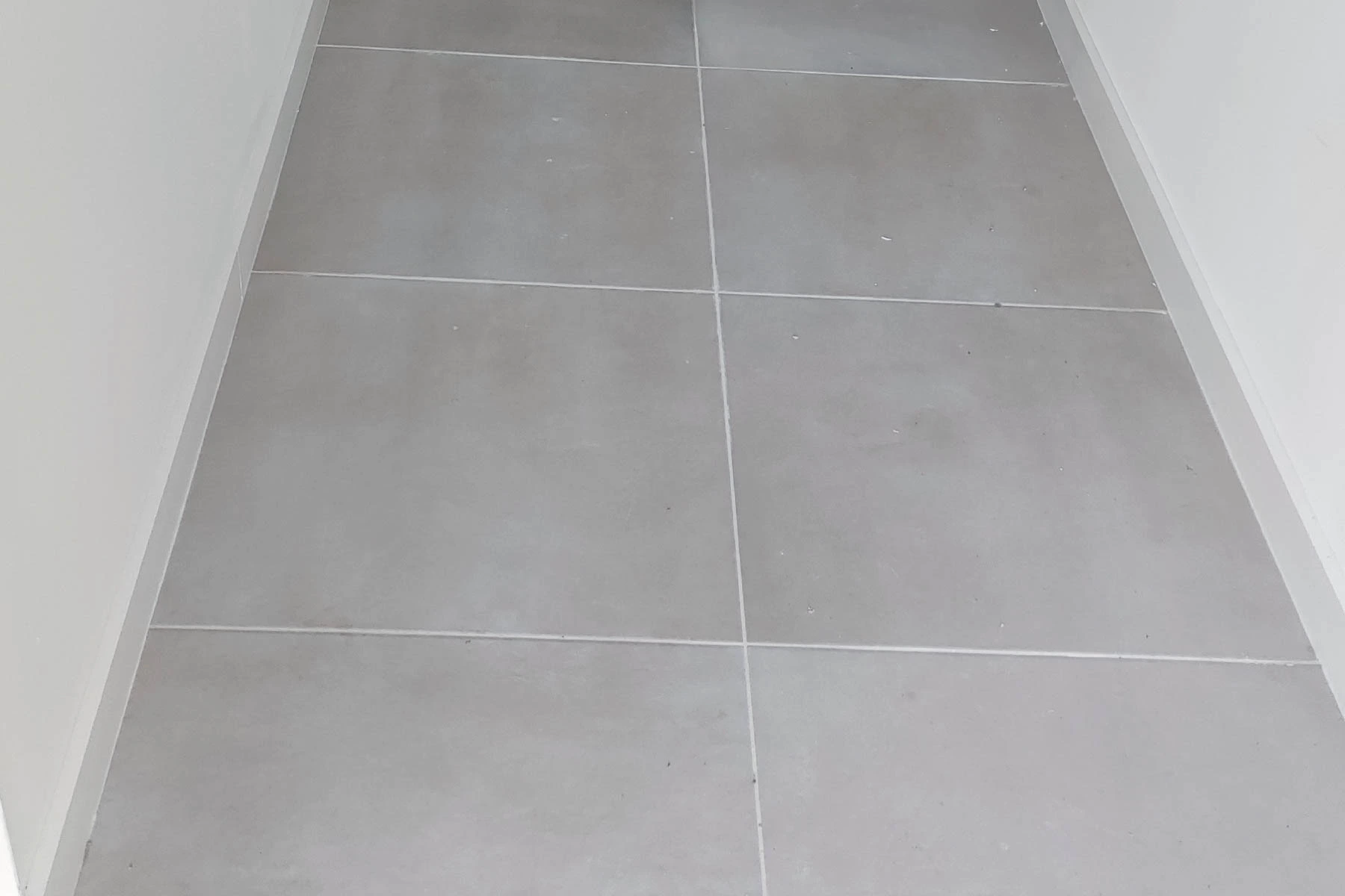 Gros plan sur la pose soignée d'un carrelage gris moderne avec plinthe assortie, réalisée par un artisan à Nancy